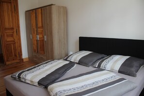 Un dormitorio con cama, dos almohadas, un armario de madera y una mesita de noche.