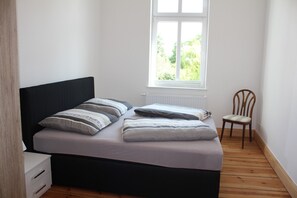A bedroom with a bed, pillows, a chair, a window, and a radiator. - Apartment 'Ferienwohnung Eg Rechts - Lychen' with Lake View, Shared Terrace and Wi-Fi (Lychen)