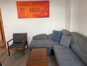 Olohuoneessa on harmaa sohva, puinen sohvapöytä, puinen nojatuoli ja seinällä punainen abstrakti maalaus.