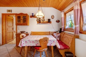 Une pièce chaleureuse avec un plafond en bois, une table à manger avec des chaises, un banc, un luminaire suspendu et une fenêtre avec des rideaux.
