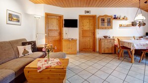Ein gemütliches Wohnzimmer mit einer Couch, einem Couchtisch, Holzschränken, einem Fernseher und einer Essecke mit Tisch und Stühlen.