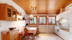 Eine Küche mit Holzausstattung, einem Esstisch mit Stühlen, einer Pendelleuchte und einem Fenster mit Vorhängen.