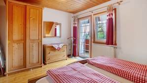 Ein Zimmer mit Holzböden, einem Holzschrank, einem Schminktisch, einem Spiegel, zwei Betten mit karierter Bettwäsche und einem Fenster mit Vorhängen.