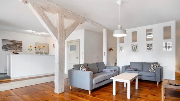 Ein modernes Wohnzimmer mit Holzboden, zwei grauen Sofas, einem weißen Couchtisch und einer Küchenzeile im Hintergrund.
