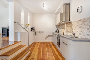 A modern kitchen with wooden flooring, white cabinetry, a stainless steel sink, and a clock on the wall. - Apartment 'Alte Seifensiederei 2' with Wi-Fi (Stralsund)