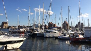 Ein Yachthafen mit mehreren vertäuten Booten, blauem Himmel und Gebäuden im Hintergrund.