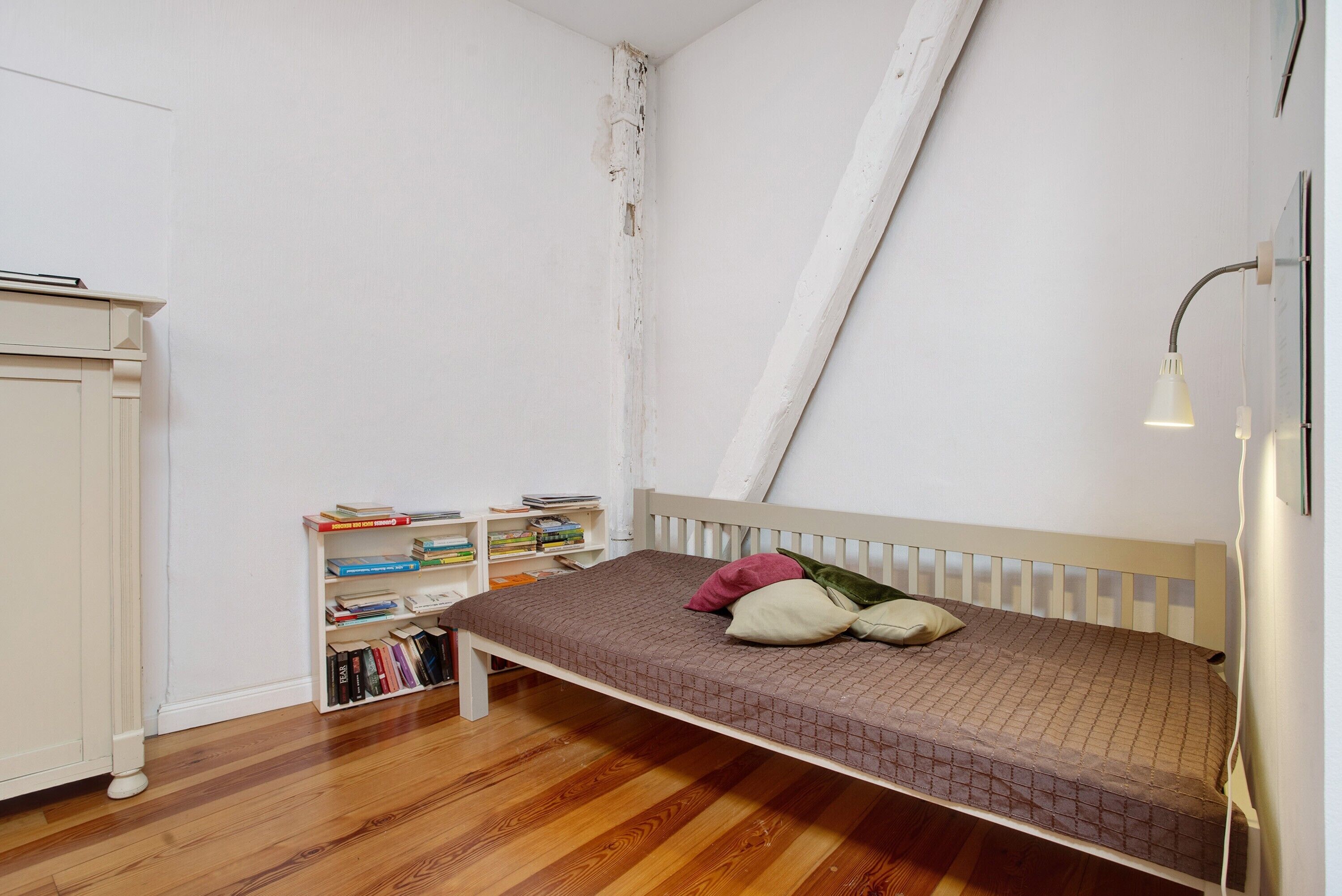 Un dormitorio con una cama individual, una estantería y un armario blanco.