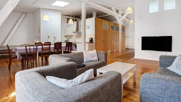 A modern living room with grey sofas, a white coffee table, and a dining area with wooden chairs and a table. - Holiday Apartment 'Alte Seifensiederei - Ferienloft' with Wi-Fi (Stralsund)