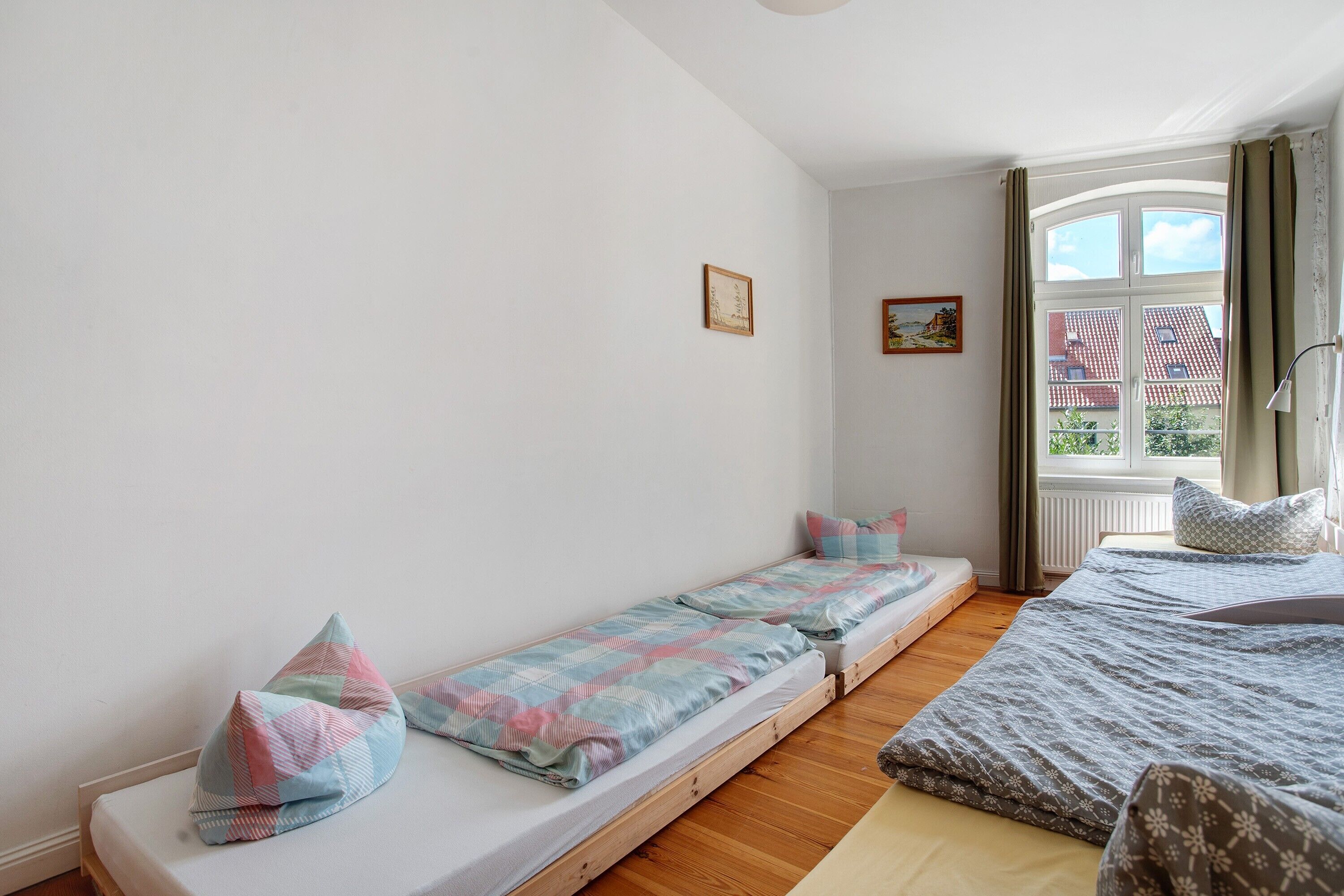 Una habitación con cama, ventana con cortinas, radiador y un cuadro en la pared.