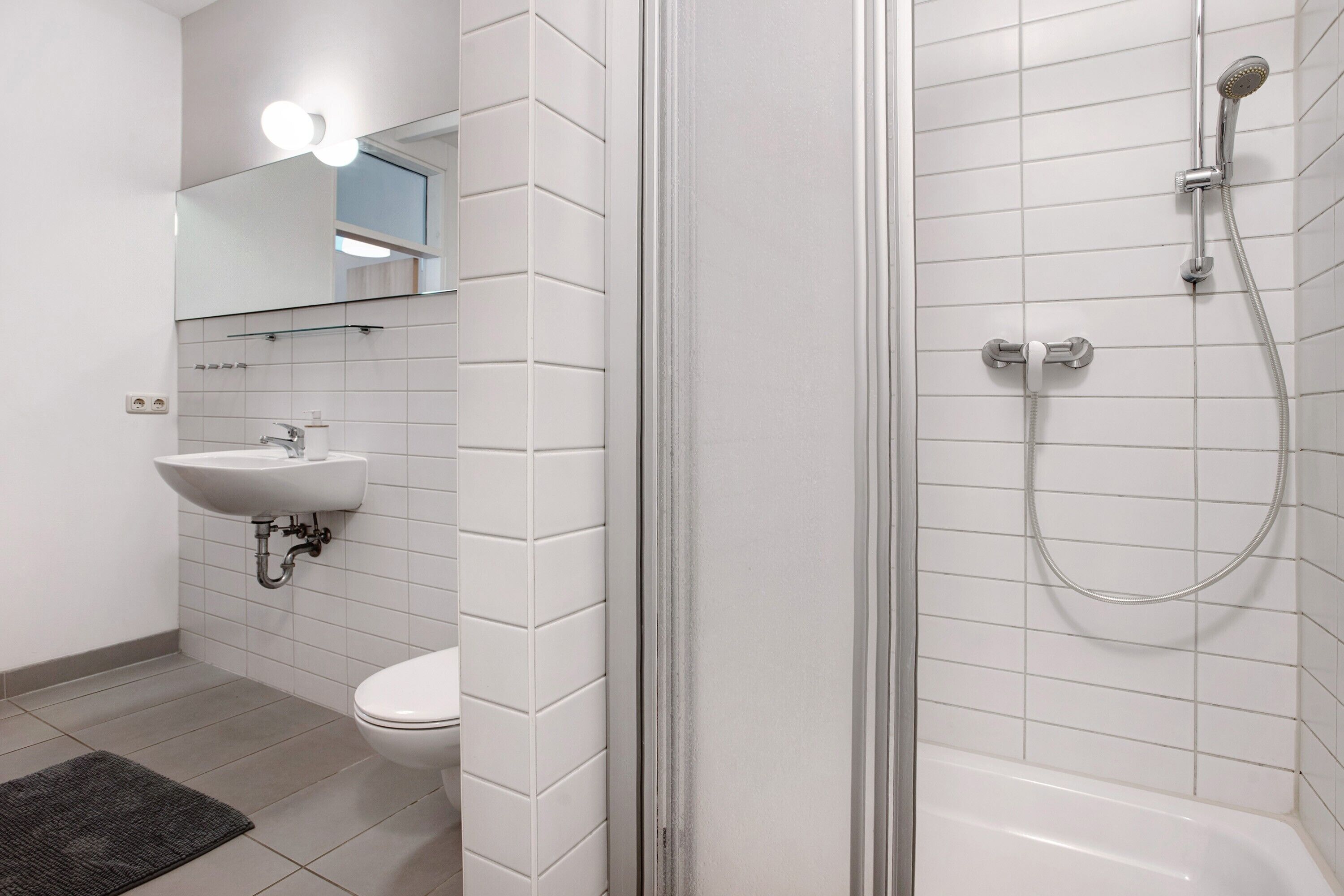 A bathroom with a sink, toilet, mirror, and shower.