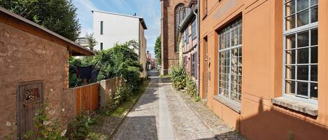 Un estrecho callejón empedrado flanqueado por edificios, incluyendo una construcción de ladrillo con una ventana y un edificio blanco con una puerta.