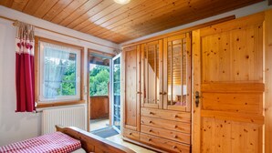 Habitación con paneles de madera, un armario grande, dos camas con ropa de cama a cuadros y una ventana con vistas a follaje.