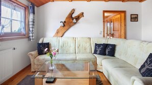 Una sala de estar con un sofá de color claro, una mesa de centro de vidrio, un techo de madera y una gran escultura de madera.