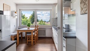 Eine moderne Küche mit Esstisch, Stühlen, einem Kühlschrank und einem Fenster mit Blick auf Bäume.