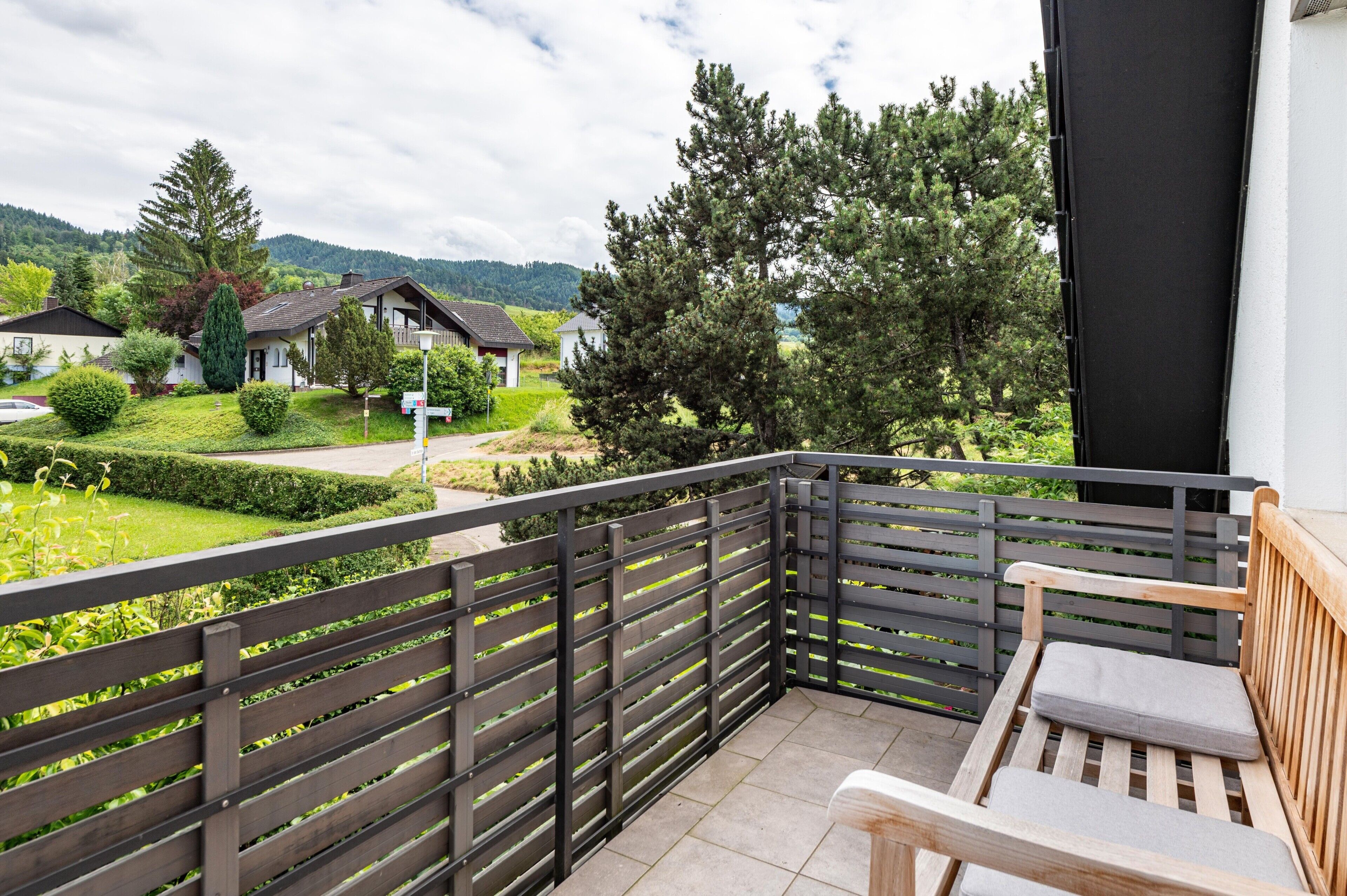 A balcony with a wooden bench, a metal railing, and a view of houses and trees.