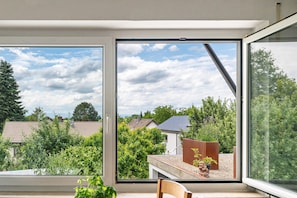 A room with a large window offering a view of a residential area, a small table, and a chair.