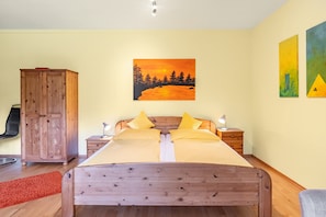 A bedroom with a wooden bed, a nightstand with a lamp, a wardrobe, and a painting of a sunset on the wall. - Apartment 'Donnerberg' with Shared Terrace, Shared Garden and Wi-Fi (Ühlingen-Birkendorf)