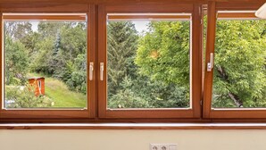 A window with three panes, a wooden frame, and a view of a green landscape with trees and a small structure. - Apartment 'Donnerberg' with Shared Terrace, Shared Garden and Wi-Fi (Ühlingen-Birkendorf)