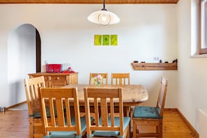 Zona pranzo con tavolo e sedie in legno, lampadario a sospensione e mensola a muro con pigne.