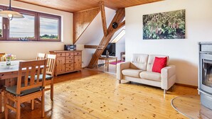 A wooden interior with a dining table, chairs, a sofa, a fireplace, and a painting on the wall. - Apartment 'Hermanschau' with Shared Terrace, Shared Garden and Wi-Fi (Ühlingen-Birkendorf)