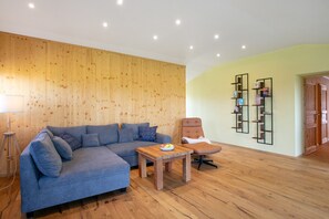 A modern living room with a sectional sofa, a wooden coffee table, a recliner, and a bookshelf.