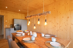 A wooden interior with a dining table set for four, a kitchen area, and a hanging light fixture.