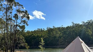 Una carpa montada en una playa arenosa, con un lago y árboles de fondo.