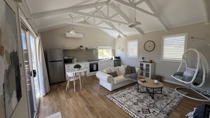 Un amplio salón con cocina, un sofá blanco, una silla colgante y una alfombra estampada.