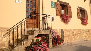 Un edificio rústico con escaleras de piedra, contraventanas de madera y jardineras con flores.