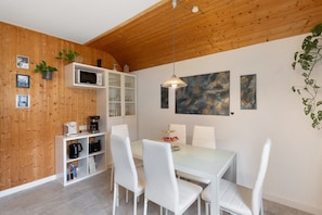 A modern kitchen with white cabinetry, a microwave, and a dining area with white chairs and a glass table. - Apartment 'Ferienwohnung Wintereck' with Mountain View (Bühlertal)