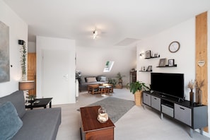 A modern living room with a sofa, coffee table, TV stand, and a dining area with a table and chairs. - Apartment 'Ferienwohnung Wintereck' with Mountain View (Bühlertal)