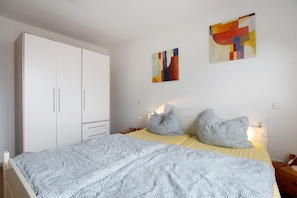 Ein Schlafzimmer mit einem Bett, einem Kleiderschrank und zwei abstrakten Bildern an der Wand.