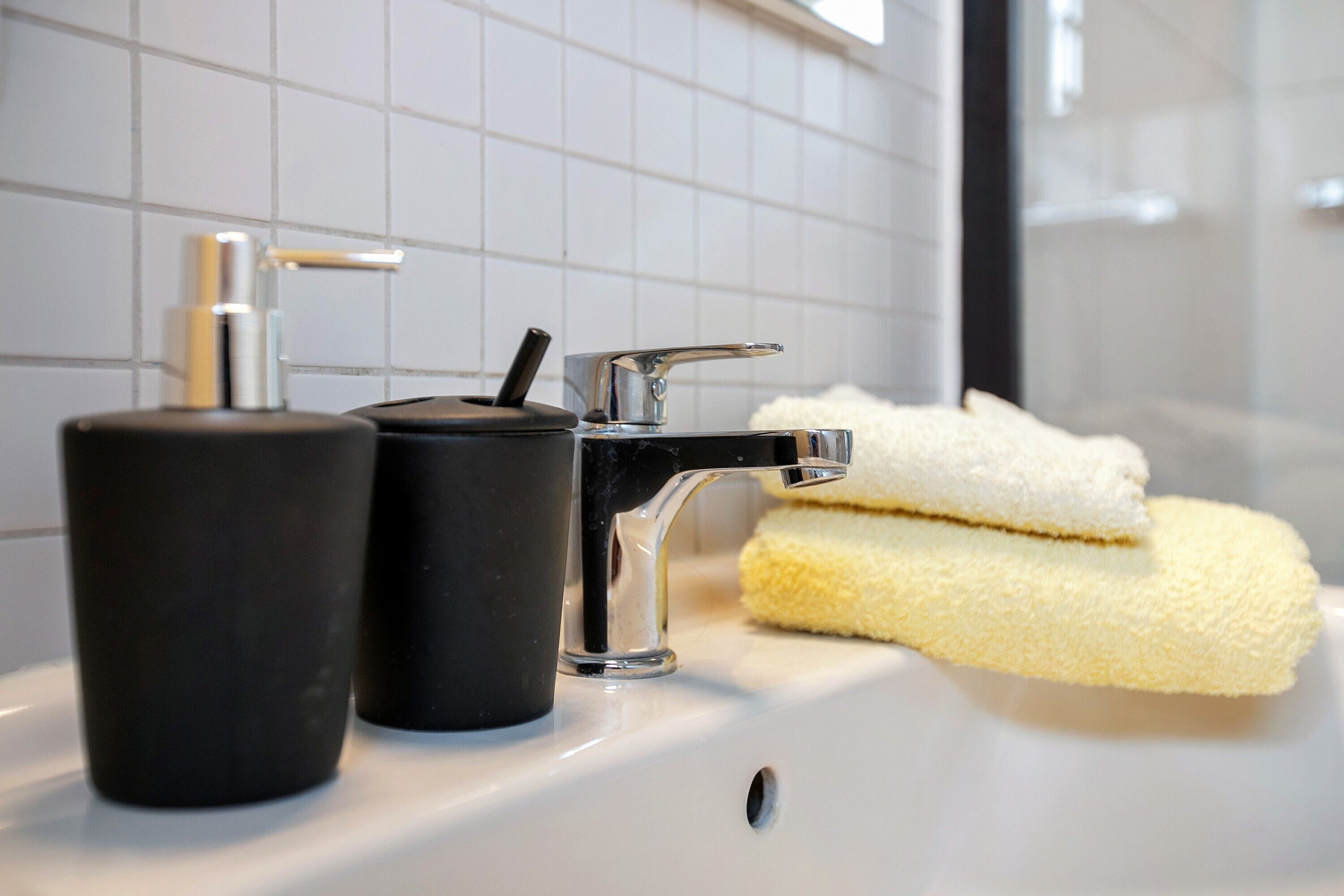 A bathroom sink with a chrome faucet, a black soap dispenser, and a yellow sponge.