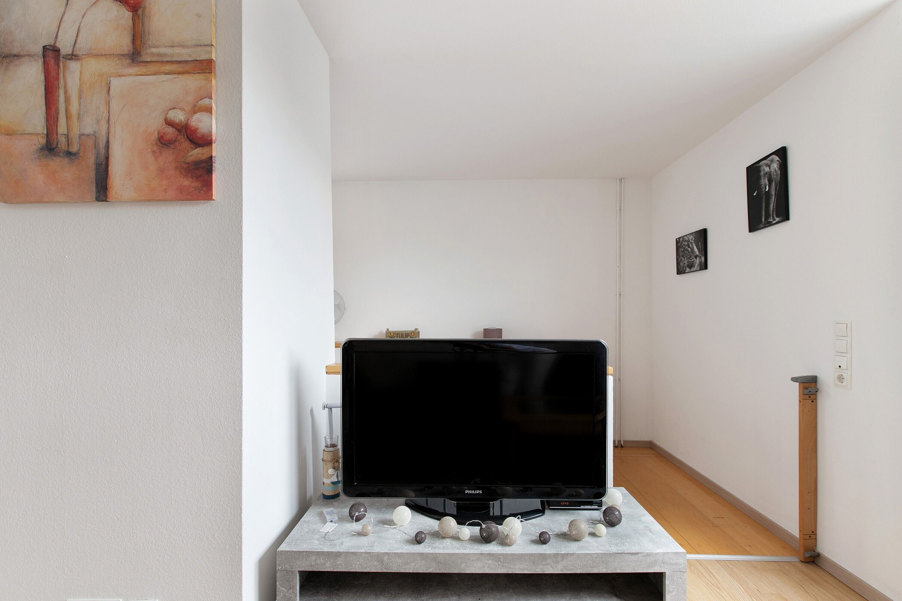 Ett vardagsrum med en tv på ett tv-bord, en tavla på väggen och ett trägolv.