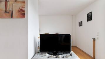 Ett vardagsrum med en tv på ett tv-bord, en tavla på väggen och ett trägolv.