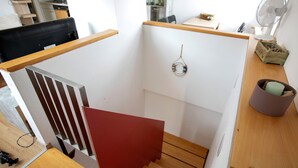 Una escalera con barandilla roja, piso de madera y pared blanca.