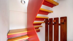 Una escalera con peldaños alternados en rojo y amarillo, barandillas de madera y una pared blanca.
