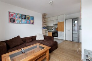 Ein modernes Wohnzimmer mit einem braunen Sofa, einem Couchtisch mit Glasplatte und einer Küche im Hintergrund.