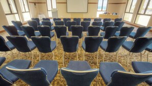 A conference room with rows of blue chairs, a projector screen, and a table with floral arrangements. - Grand Tala Bay Resort (Aqaba)