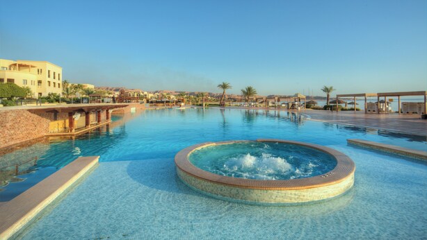 A large outdoor swimming pool with a hot tub in the center, surrounded by lounge areas and palm trees. - Grand Tala Bay Resort (Aqaba)