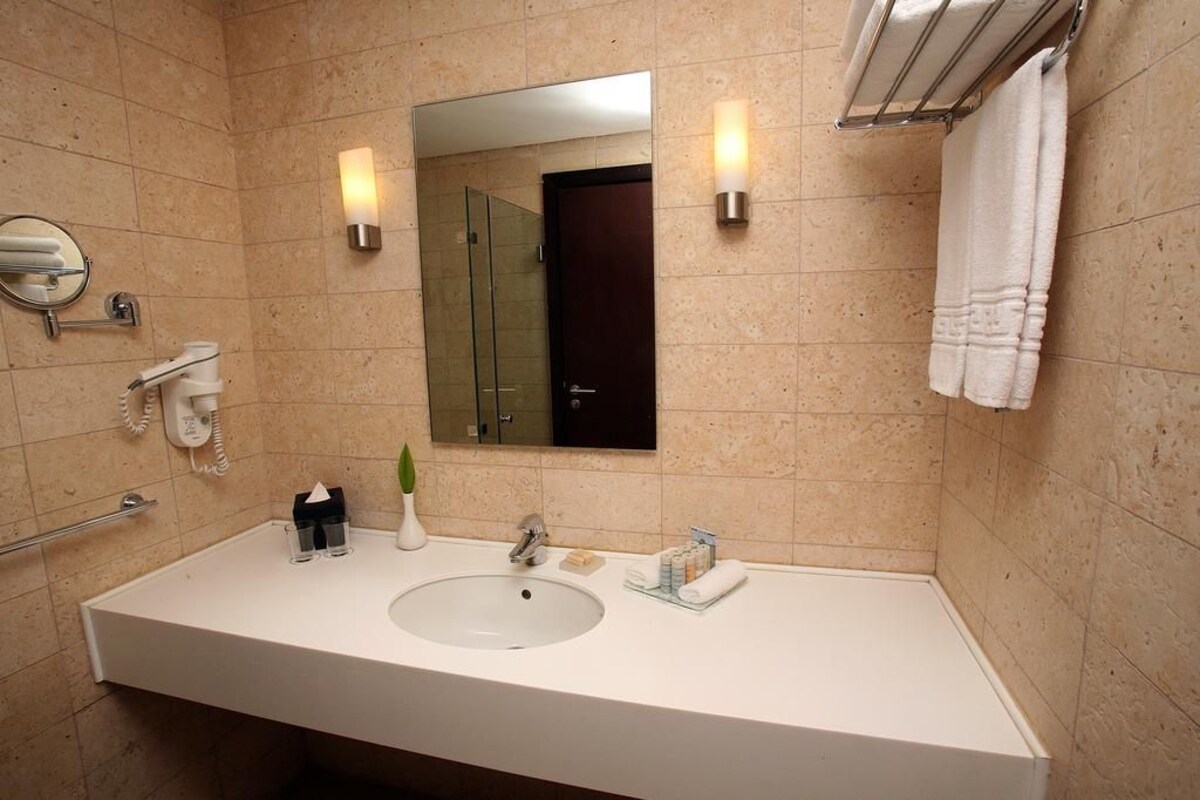 Une salle de bain avec un lavabo blanc, un miroir, un porte-serviettes et une cabine de douche en verre.