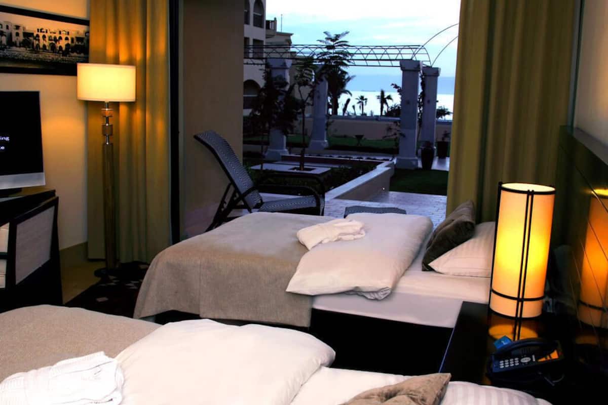 Habitación de hotel con dos camas, televisión, lámpara y vista a la piscina y palmeras.