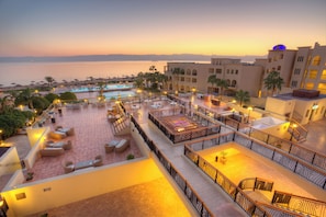 A rooftop terrace with outdoor seating, a pool, and a view of the sea at sunset.