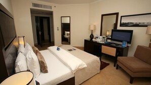 A hotel room with a bed, a desk with a TV, a chair, and a mirror. - Grand Tala Bay Resort (Aqaba)