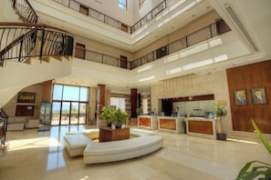 A spacious lobby with a curved seating area, a reception desk, and a staircase leading to upper floors.