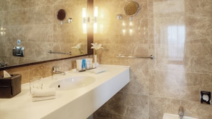 A modern bathroom with a large mirror, a white sink, a bidet, and marble walls.