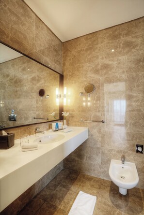 A modern bathroom with a large mirror, a white sink, a bidet, and marble walls.