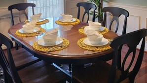 A dining room with a wooden table set for four, surrounded by chairs.