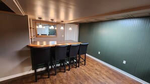 A kitchen with a wooden countertop, four black bar stools, pendant lights, and a green textured wall.