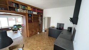 Ein geräumiger Wohnbereich mit einer Holzbücherwand, einem Esstisch und einer Küchenzeile mit modernem Spülbecken und Kaffeemaschine.